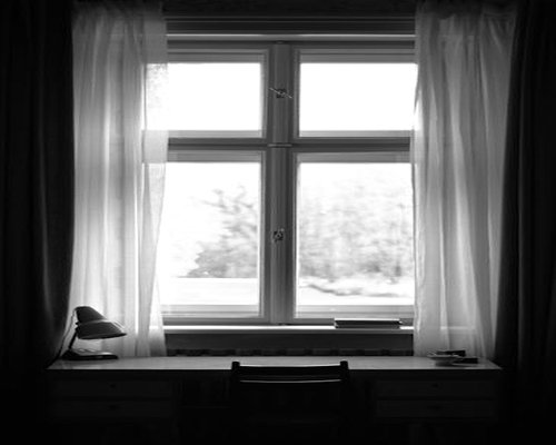Home office desk positioned perpendicular to a bright window with sheer curtains