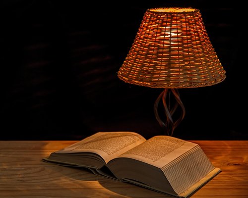 Cozy reading corner with an open book illuminated by a warm yellow desk lamp